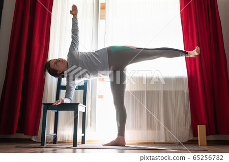 yoga student standing in ardha chandrasana or Half Moon Pose leaning on chair yoga student standing in ardha chandrasana or Half Moon Pose leaning on chair 65256782
