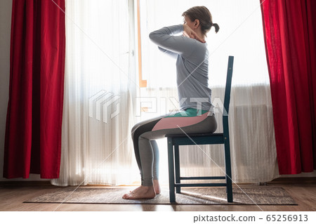 Beautiful young girl doing exercises at home using chair. 65256913