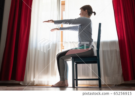 Beautiful young girl doing exercises at home using chair. 65256915