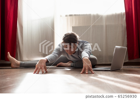 woman practicing yoga, doing Janu Sirsasana variation at the living room at home woman practicing yoga, doing Janu Sirsasana variation at the living room at home 65256930