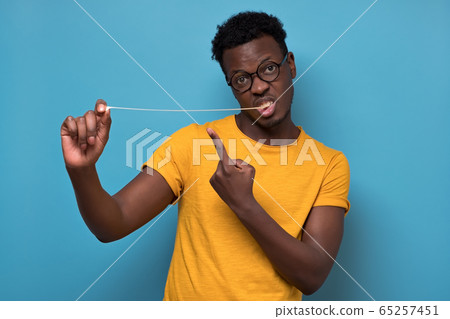 Young african american man in a studio, pulling a chewing gum. 65257451