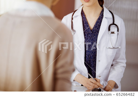 Doctor and patient discussing current health examination while sitting in sunny clinic. Perfect medical service in hospital Doctor and patient discussing current health examination while sitting in sunny clinic. Perfect medical service in hospital 65266482