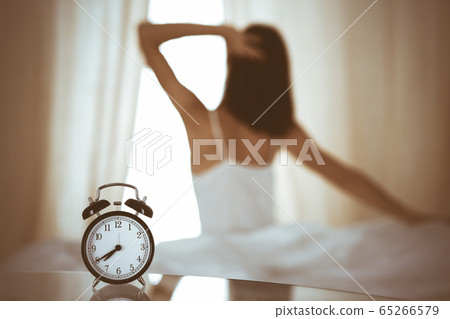 Woman stretching hands in bed after wake up, sun flare . Brunette entering a day happy and relaxed after good night sleep and back view. Concept of a new day and joyful weekend 65266579
