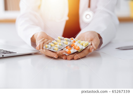 Unknown woman-doctor offering pack of different tablet blisters in sunny room, close-up Unknown woman-doctor offering pack of different tablet blisters in sunny room, close-up 65267339