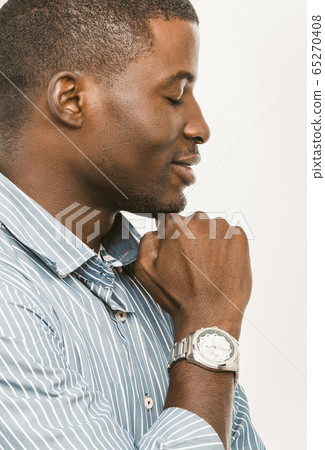 Chilling Afro-American businessman shows his wrist watch. Profile portrait of intelligent dark-skinned businessman closing his eyes and smiling with clock on hand. Close up shot Chilling Afro-American businessman shows his wrist watch. Profile portrait of intelligent dark-skinned businessman closing his eyes and smiling with clock on hand. Close up shot 65270408