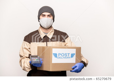 Young male courier in workwear holding big carton box and payment terminal Young male courier in workwear holding big carton box and payment terminal 65270679