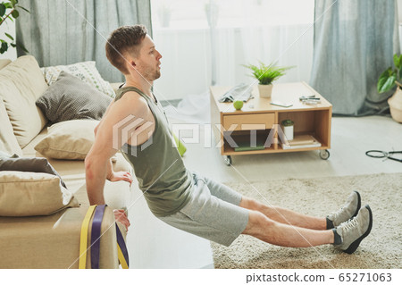 Sweaty athlete in sportswear holding by couch behind his back while exercising 65271063