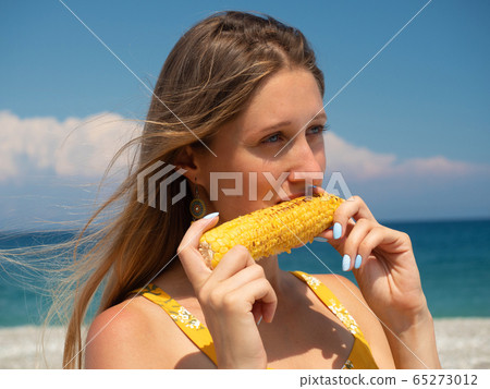 Young woman eating corn on the beach Young woman eating corn on the beach 65273012