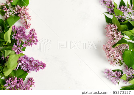 Greeting frame from fresh lilac flowers with green leaves on a light grey marble background. Top view. 65273137