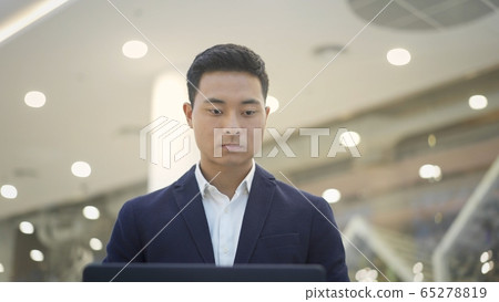 front view of asian male businessman in suit working with laptop on his knees front view of asian male businessman in suit working with laptop on his knees 65278819