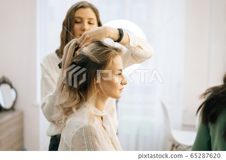 Two make-up artistes applies hair and makeup to the bride in dressing room. 65287620