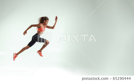 Never give up. Full length of young african woman with perfect body in sports clothing jumping in studio against grey background Never give up. Full length of young african woman with perfect body in sports clothing jumping in studio against grey background 65290444