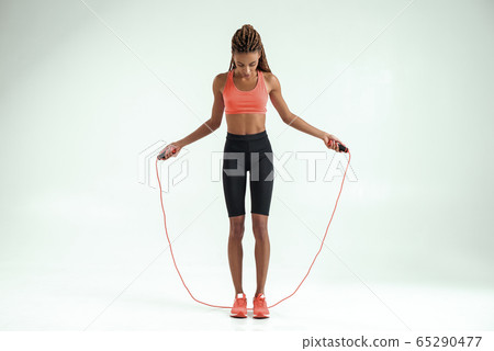 Perfect body. Full length of beautiful african woman in sportswear skipping rope while exercising in studio against grey background Perfect body. Full length of beautiful african woman in sportswear skipping rope while exercising in studio against grey background 65290477