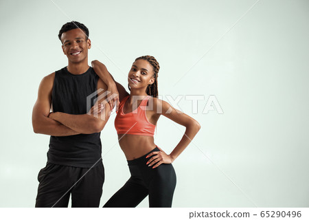 Sporty and healthy. Young african fitness couple in sportswear looking at camera and smiling while standing against grey background Sporty and healthy. Young african fitness couple in sportswear looking at camera and smiling while standing against grey background 65290496