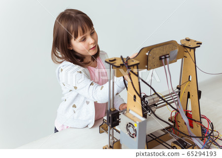 Cute girl with 3d printed shutter shades is watching her 3d printer as it prints her 3d model. 65294193