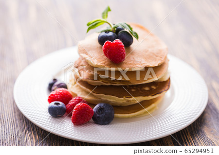 Pile of pancakes with blueberries and raspberries for breakfast on wooden table. Pile of pancakes with blueberries and raspberries for breakfast on wooden table. 65294951