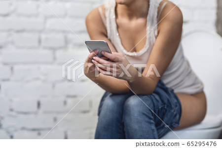 Woman With Smartphone Playing Mobile Games Sitting On Toilet, Cropped Woman With Smartphone Playing Mobile Games Sitting On Toilet, Cropped 65295476