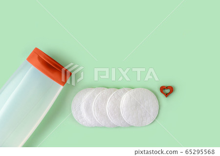 Cleansing tonic in a translucent jar, few cotton pads and small wood heart on a pastel mint Cleansing tonic in a translucent jar, few cotton pads and small wood heart on a pastel mint 65295568