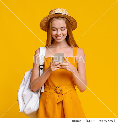Travel Sim Concept. Girl Tourist With Backpack Using Smartphone Over Yellow Background Travel Sim Concept. Girl Tourist With Backpack Using Smartphone Over Yellow Background 65296291