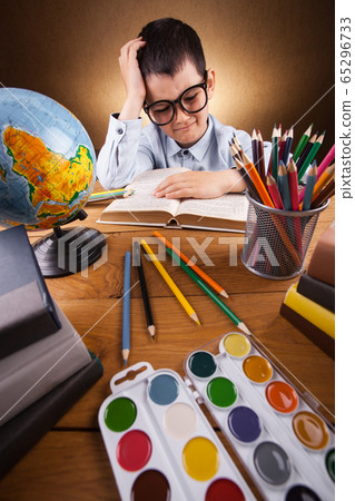 cute little boy schoolboy doing homework at a table with books cute little boy schoolboy doing homework at a table with books 65296733