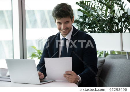 Businessman sitting at desk in office holding papers read report Businessman sitting at desk in office holding papers read report 65298496