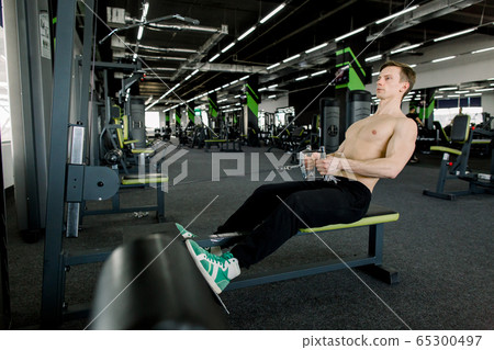 Fitness young man using rowing machine in the gym. Sporty man in the gym 65300497