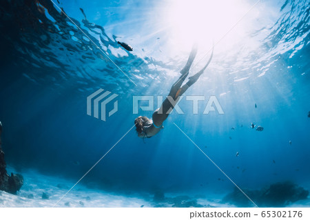 Woman free diver with fins glides over sandy bottom near corals underwater in blue ocean 65302176