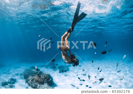 Free diver girl with fins glides over sandy bottom with tropical fishes in blue ocean Free diver girl with fins glides over sandy bottom with tropical fishes in blue ocean 65302178