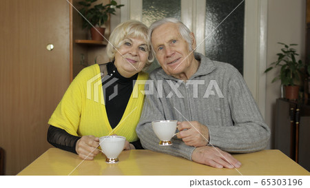 Happy old grandparents couple sit on table at home enjoy drinking tea together Happy old grandparents couple sit on table at home enjoy drinking tea together 65303196