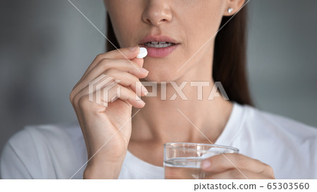 Cropped closeup image woman taking pill holding glass of water 65303560