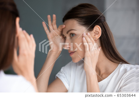 Satisfied woman looking in mirror check face after beauty treatment 65303644