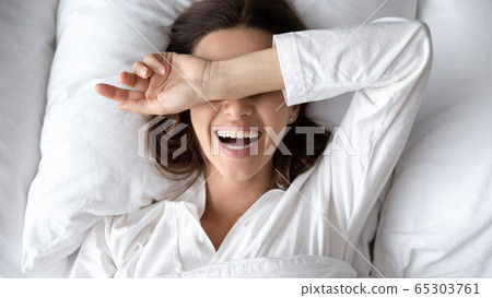 Woman with toothy smile wokeup after sleeping lying in bed 65303761