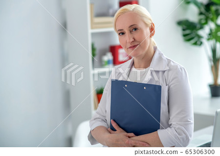 Blonde middle-aged doctor holding documents and looking positively 65306300