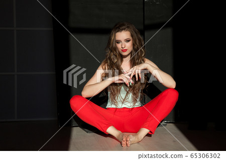 Portrait of a beautiful fashionable woman with hair curls in red trousers Portrait of a beautiful fashionable woman with hair curls in red trousers 65306302