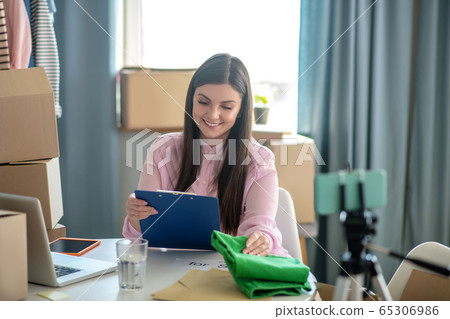 Dark-haired young woman looking at the list and smiling Dark-haired young woman looking at the list and smiling 65306986