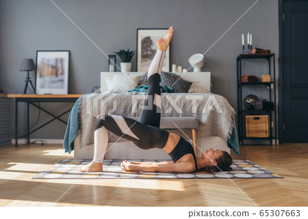 Fit woman trains at home and does exercise glute bridge. 65307663