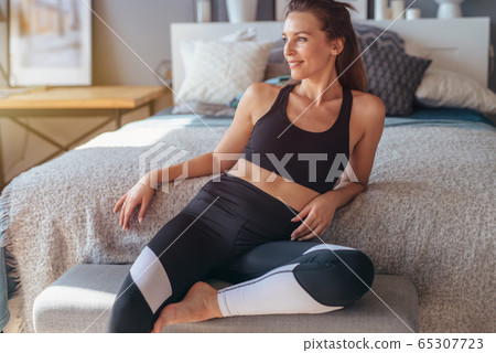 Portrait of young female athlete at home. Woman sitting relaxed before workout in bedroom 65307723
