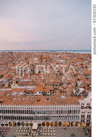 Panoramic view of the island city of Venice in Italy, from the huge tower on the San Marco square, onto the roofs of buildings through the clock tower of St. Mark. 65308330