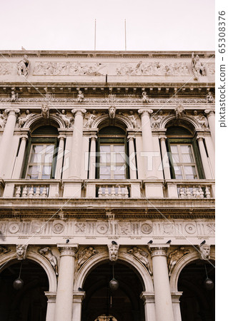 Vintage ornate windows and columns, venetian style, on fragment of building's luxurious building in Venice. Traditional ancient gothic style. Three windows and arches decorated with stucco molding. 65308376