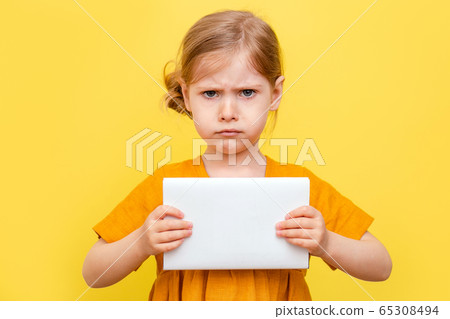 A little girl with light hair on a yellow background. Isolated. A child in a yellow dress makes notes on a book. Mockup. A little girl with light hair on a yellow background. Isolated. A child in a yellow dress makes notes on a book. Mockup. 65308494