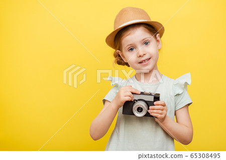 A little girl in a straw hat with a camera in her hands on a yellow isolated background. Space for text. A little girl in a straw hat with a camera in her hands on a yellow isolated background. Space for text. 65308495