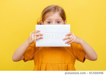 A little girl with light hair on a yellow background. Isolated. A child in a yellow dress makes notes on a book. Mockup. A little girl with light hair on a yellow background. Isolated. A child in a yellow dress makes notes on a book. Mockup. 65308496