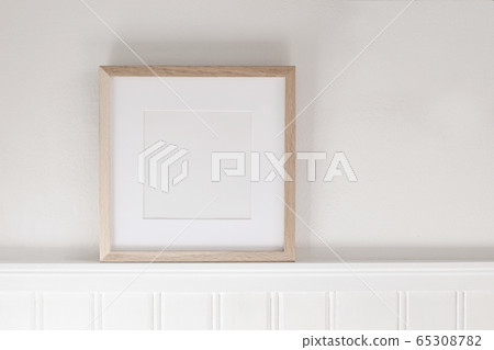 Closeup of square empty wooden picture frame on shelf. White beadboard wainscot wall paneling background. Scandinavian interior, home design. Art concept. Artistic mockup scene. Front view. Closeup of square empty wooden picture frame on shelf. White beadboard wainscot wall paneling background. Scandinavian interior, home design. Art concept. Artistic mockup scene. Front view. 65308782