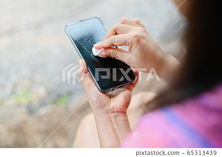 Cleaning smartphone screen with alcohol spray and cloth wet wipes to remove bacteria and dirt preventive wiping for COVID-19 Coronavirus outbreak contamination prevention 65313439