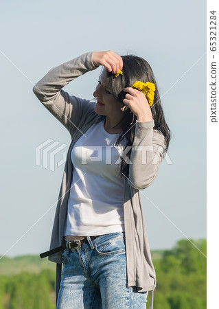 a beautiful girl, a brunette, stands in a flower meadow and adjusts dandelions in her hair 65321284