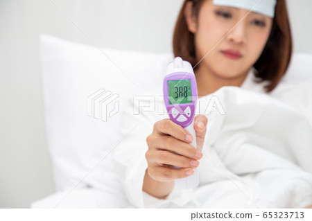 Young Asian woman holding digital thermometer with Young Asian woman holding digital thermometer with 65323713
