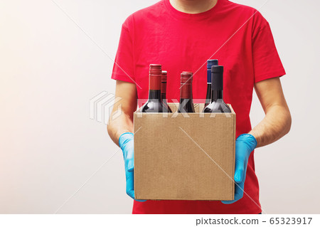 Courier wearing protective gloves holding box with bottles of wine. Courier wearing protective gloves holding box with bottles of wine. 65323917