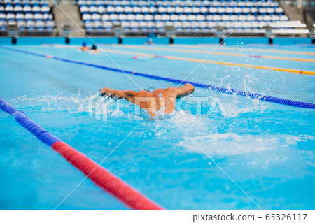 Athletic man swimming in butterfly style in the swimming pool with clear blue water. 65326117