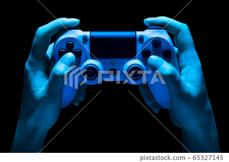 Hyman hands holding white video game gamepad in neon lights isolated on a black 65327145