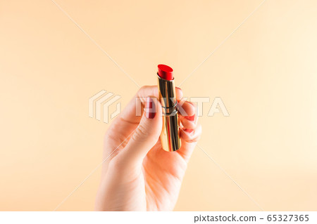 Female hand holding red lipstick on light orange Female hand holding red lipstick on light orange 65327365